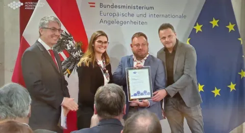 Four people pose for the camera, one of them holding an award.