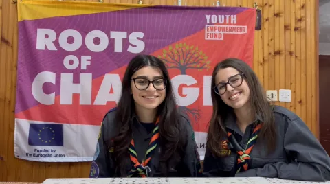 Two girls, wearing Scout scarves, smile at the camera.