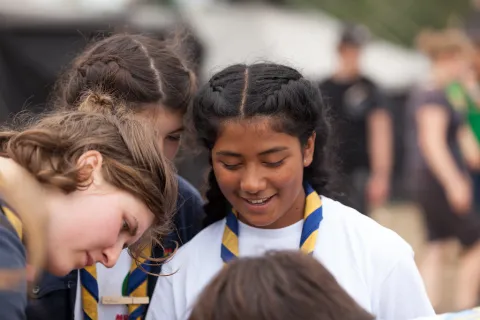 Young girls wearing scarves smile at something not visible in the image.