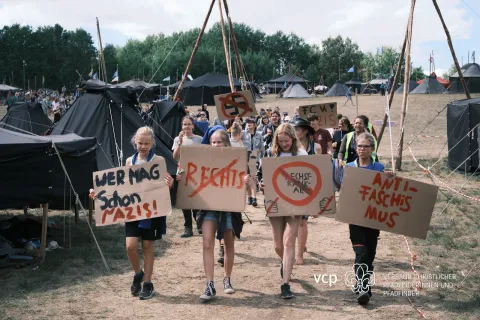 Scouts walk at a campsite holding banners.