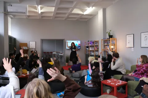 Youth seat on the ground raising one of their arms while an activist speaks in front of them.