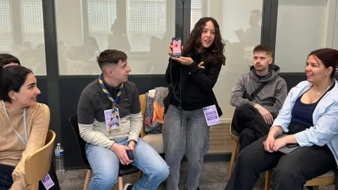 A young girl shows the screen of her phone while youth around her look at it.