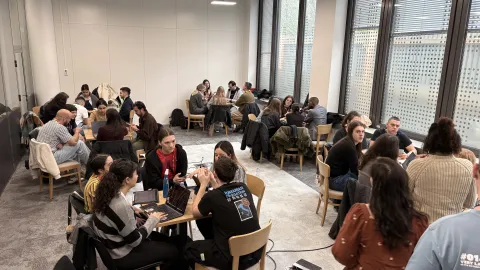 Young people seat grouped around several tables in a room.