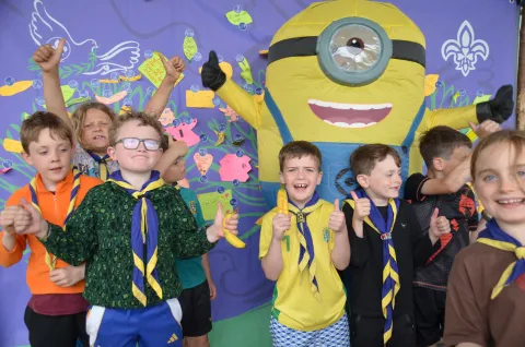 Children smile and hold bananas in front of a banner, together with someone in a minion costume.