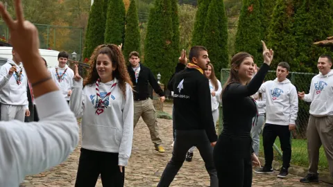 Young people wearing Scout scarves stand making two circles and gestures with their hands.