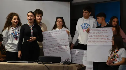 Young people stand in a room speaking while holding flipcharts.