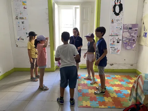 Carolina and the children stand forming a circle in a room with decorations on the walls.