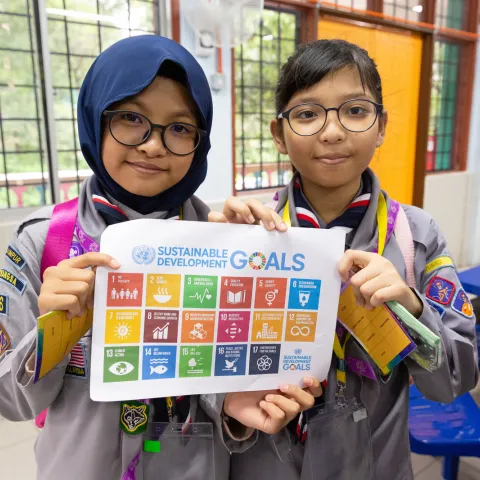 Two Malaysian Scout girls in their uniforms hols a sheet displaying the Sustainable Development Goals during JOTA-JOTI